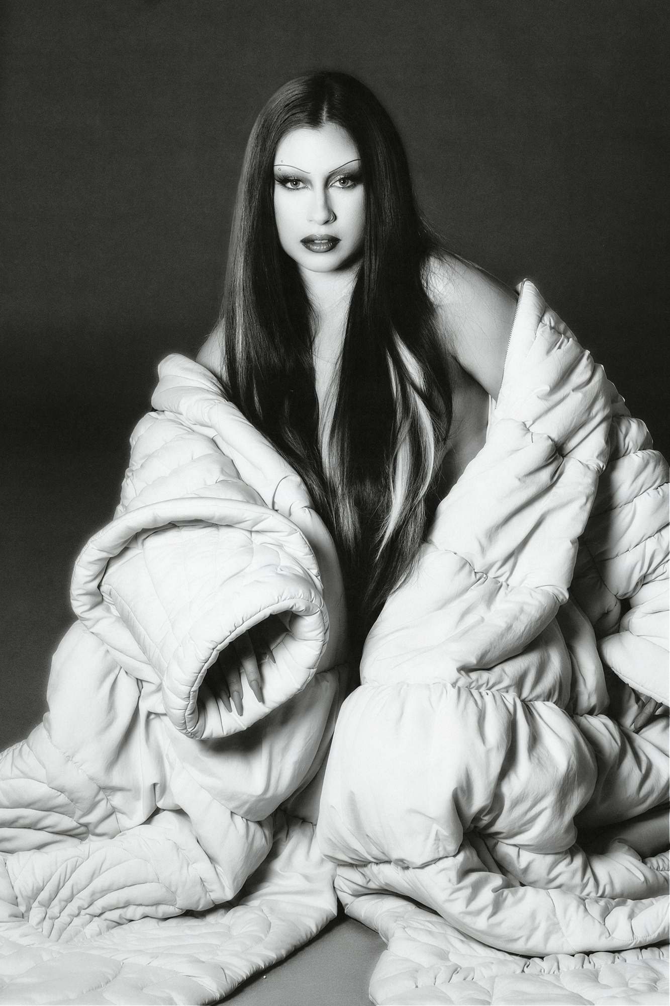 Black and white image of Lauren Juaregui in a large white down coat hanging off her shoulder looking towards the camera